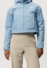 Blå kort jacka med huva, dragkedjestängning och vitt logo på bröstet; designad med en slät yta och lätt material.