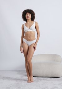 Λευκό σετ εσωρούχων με μαλακό σουτιέν με κυματοειδείς άκρες και αντίστοιχες βερμούδες. Λείο ύφασμα με ελαφριά λάμψη, μίνιμαλ σχέδιο και χωρίς μοτίβα.