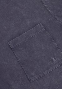 Tela de algodón azul oscuro con un acabado texturizado, que presenta un bolsillo frontal y un logo sutil en relieve. Diseño simple y casual.