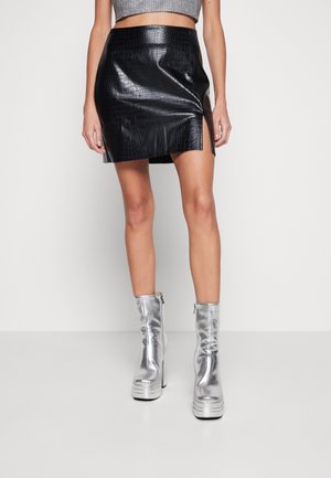 Black faux crocodile leather mini skirt with front slit worn with silver platform ankle boots on bare legs.