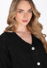 Cardigan nero a maglia con un motivo testurizzato, design a V, e tre bottoni argentati sul davanti, realizzato in un tessuto morbido e accogliente.