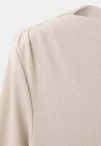 Gros plan sur un tissu côtelé beige montrant les détails des coutures aux épaules et dans le haut du dos d’un vêtement en maille.