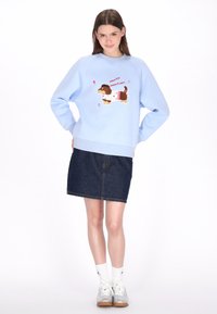 Világoskék pulóver kutyás grafikával, pöttyökkel és szöveggel. Sötét farmer szoknyával és fehér zoknival párosítva, ezüst tornacipőkkel kiegészítve.