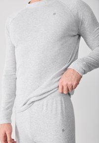 Ljusgrå långärmad topp med raglanärmar, rundad halsringning och logotyp på bröstet. Matchande ljusgrå byxor. Mjuk tygkänsla.