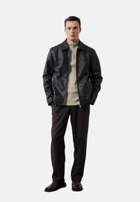 Zwarte leren jas met een rits, gecombineerd met een beige geribde trui en donkere broek. Eenvoudig ontwerp met een kraag.