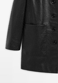 Manteau en cuir noir à surface texturée, doté d'une grande poche, de revers arrondis et d'une fermeture à boutons. Matériau lisse et durable.