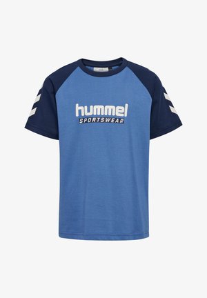 To børn iført blå og marineblå hummel sportst-shirts og vinrøde bukser står mod en ensfarvet lys baggrund.