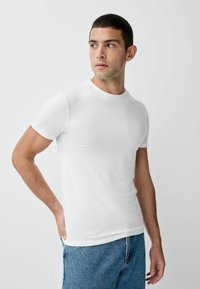 Balta kokvilnas t-krekls ar apaļu kakla izgriezumu un īsām piedurknēm, pieguļošs dizains, valkāts kopā ar ziliem džinsa džinsiem, gluda tekstūra.