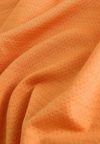 Tessuto arancione testurizzato con motivo traspirante a piccoli fori, che mostra una caduta morbida e un colore vivace.