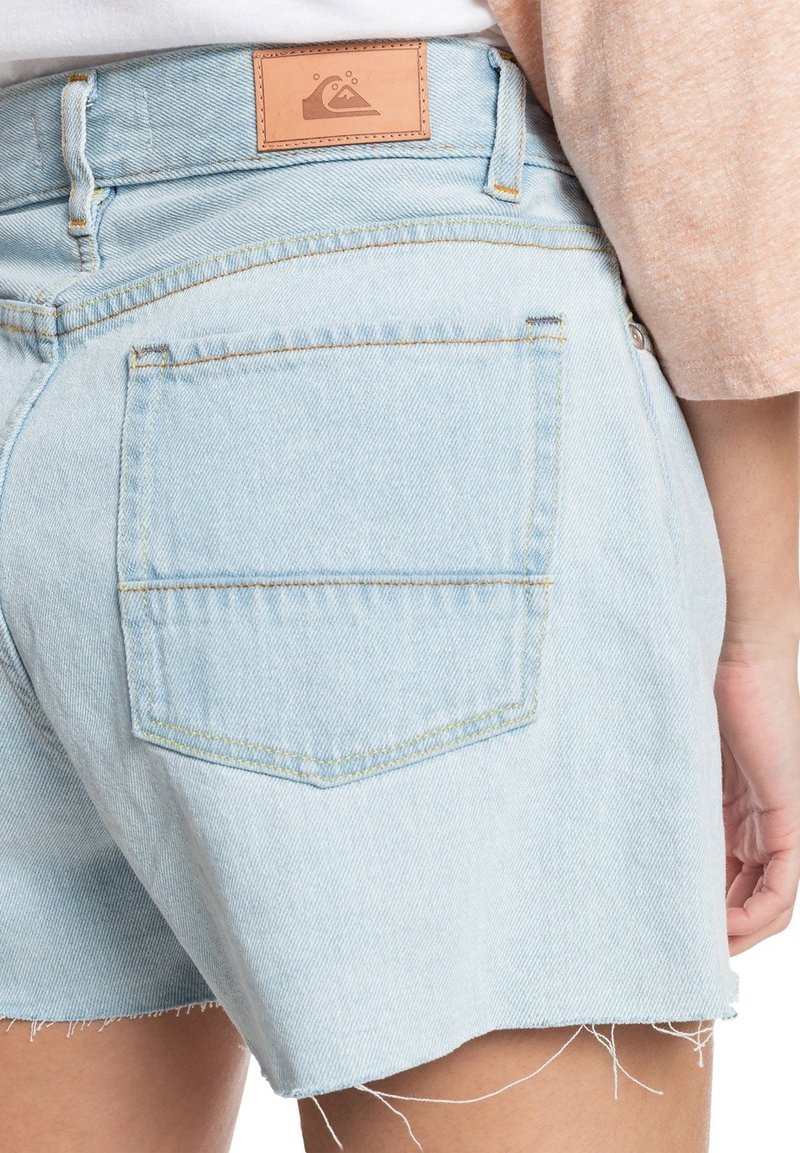 Ljust blå denimshorts med fransat fåll, stickning på bakfickorna och en brun lädertagg vid midjan med en våglogotyp.