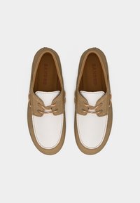 Par de zapatos náuticos de cuero marrón y blanco con detalles de cordones, vistos desde arriba sobre un fondo liso.
