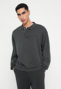 Ciemnoszary longsleeve polo z kołnierzykiem, wykonany z teksturowanej tkaniny. Posiada luźny krój i pikowane detale na brzegach.