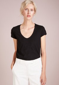 Schwarzes T-Shirt mit kurzen Ärmeln und tiefem V-Ausschnitt, präsentiert mit weißen gestreiften Hosen. Glattes, leichtes Material mit lässiger Passform.