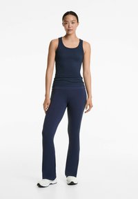 Navyblaues, geripptes Tanktop, kombiniert mit passenden, engen Hosen. Das Outfit besticht durch ein schlichtes Design und eine glatte Textur, die durch weiße Sneakers ergänzt wird.