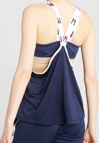 Canotta sportiva blu navy con texture a rete, spalline bianche con un motivo di logo. Design con schiena aperta che offre ventilazione e comfort.