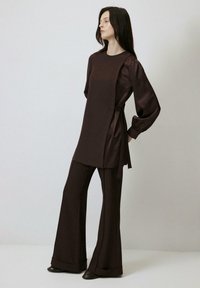 Costum din două piese, de un brun închis, satinat, care include o tunică lungă cu mâneci bufante și pantaloni largi, legat la talie cu un detaliu lateral.
