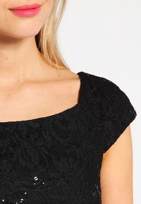 Vestito nero in pizzo con scollatura a barca e maniche corte, caratterizzato da motivi floreali e paillettes per un tocco di texture e dettaglio.
