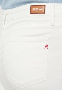 Λευκά τζιν από denim με καφέ δερμάτινο ταμπελάκι με την επιγραφή "REPLAY" και κόκκινη κεντητή λεπτομέρεια στην πίσω τσέπη. Απλός σχεδιασμός ραφής.