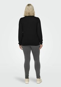 Maglione nero a maniche lunghe con scollatura rotonda, abbinato a leggings grigi e scarpe da ginnastica di colore chiaro. Texture liscia, design informale.