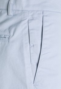 Hellblaue Baumwollhosen mit glatter Textur, ausgestattet mit einer Seitentasche und dezenten Nähten entlang der Säume.