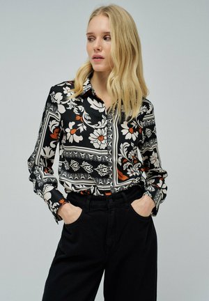 Camisa de botones negra con estampado de flores en blanco y naranja, cuello estructurado, mangas largas y detalles en los puños en contraste.