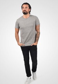 Grå mønstrete t-skjorte med korte ermer for menn, kombinert med svarte jeans og hvite joggesko. Teksturen ser myk ut; passformen er uformell og avslappet.