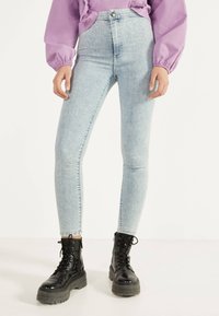 Vaaleansiniset korkeavyötäröiset skinny-farkut, joissa on haalistunut pinta, napit ja vetoketju. Yhdistetty mustiin nauhakenkiin.