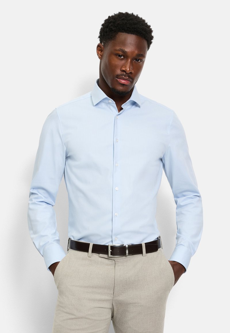 Camicia azzurro chiaro con bottoni davanti e maniche lunghe, realizzata in tessuto liscio. Presenta un colletto appuntito e una vestibilità sagomata, indossata con pantaloni beige.