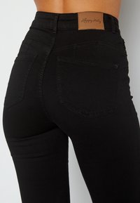 Černé džínsy s vysokým pasem vyrobené z denimu, s hnědou koženou značkou a dvěma zadními kapsami se švem.