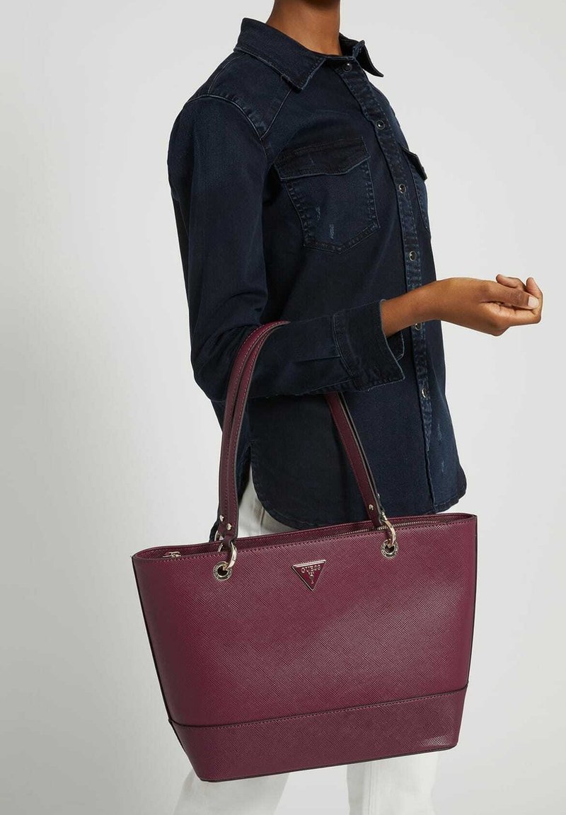Sac fourre-tout synthétique bourgogne avec surface texturée, poignées doubles et quincaillerie en argent. Présente un logo triangulaire à l'avant et un design structuré.