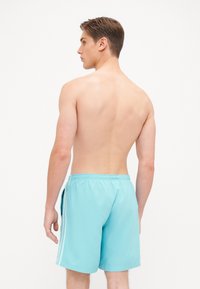 Lys blå svømmedrakt laget av glatt stoff, med elastisk midjebånd og sidelister. Designet har avslappet passform og går til kneet.
