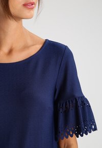 Top blu navy con scollo rotondo e maniche corte con dettagli ad occhiello scalloppati. Realizzato in tessuto texturizzato.