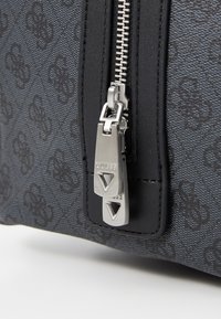 Sac à main noir à motif avec une finition texturée, fermeture éclair argentée avec tirettes de marque, et un design rectangulaire élégant.