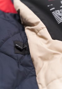 Detail einer gepolsterten Winterjacke mit einem Marineblau- und Beige-Farbschema, gestepptem Muster und einer schwarzen Zugkordel.