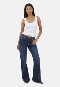 Biała bezrękawnikowa koszulka w połączeniu z ciemnoniebieskimi dżinsami w stylu dzwonów. Dżinsy mają pięć kieszeni i delikatne wyblaknięcie. Czerwone, spiczaste obcasy.