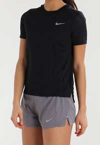 Camiseta atlética negra de Nike de manga corta con un diseño ajustado y acentos de malla, combinada con pantalones cortos grises de Nike que presentan una abertura y el logo.
