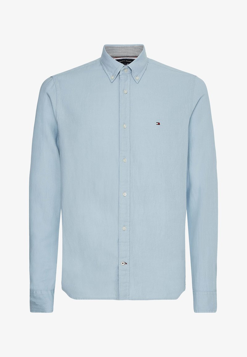 Camisa azul claro de botones hecha de tela tejida, con cuello puntiagudo, mangas largas y un pequeño logotipo en el pecho.