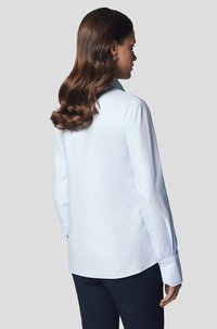 Jasnoniebieska koszula z długim rękawem, klasycznym kołnierzykiem i lekko zaokrąglonym dołem. Gładka faktura i dopasowany krój.