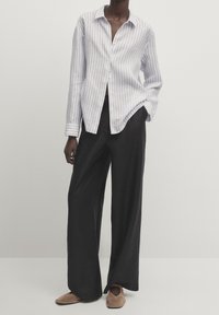 Ljusblå och vit randig skjorta med knappar och avslappnad passform, kombinerad med svarta vida byxor och taupe slip-on skor.