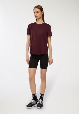 T-shirt atletico color bordeaux a maniche corte, abbinato a pantaloni sportivi neri. L'outfit presenta una vestibilità comoda, una texture liscia e un design minimale.