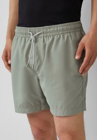 Lichtgroene zwembroek met een elastische tailleband en een trekkoord, zijzakken en een gladde, lichte textuur.