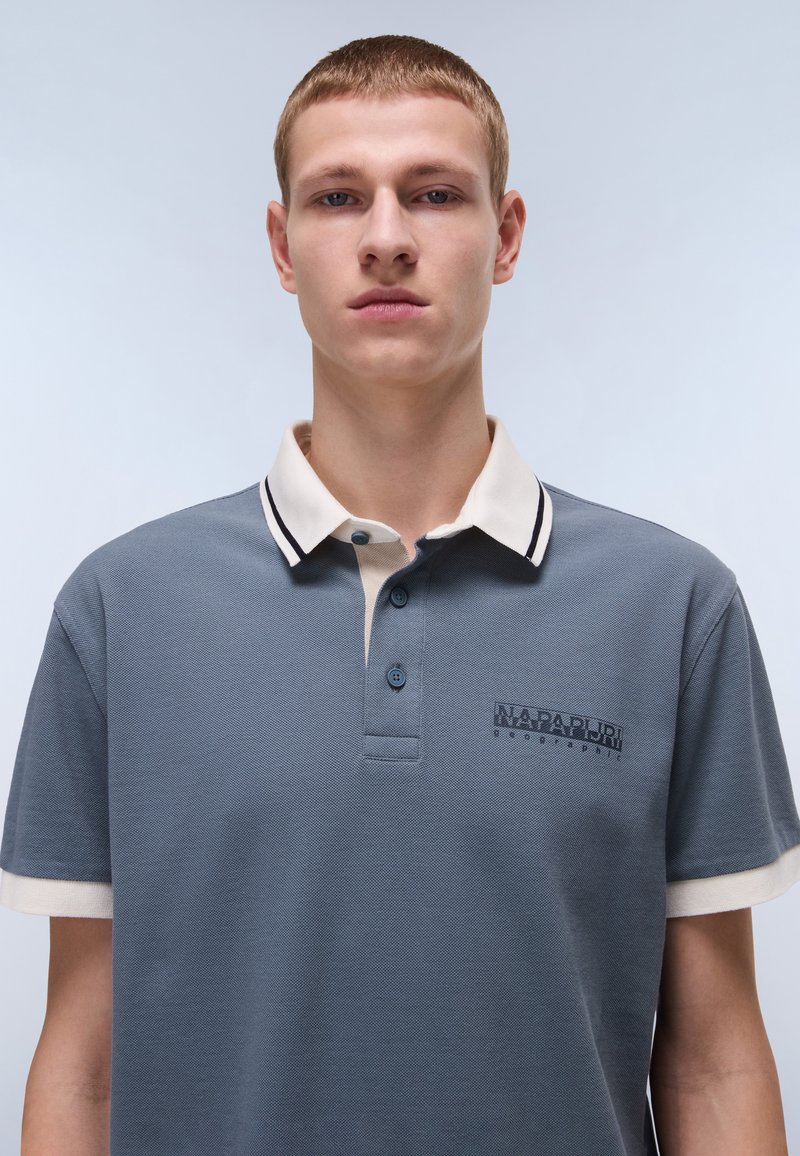 Graues Poloshirt mit einem beigen und schwarzen gestreiften Kragen, ausgestattet mit einem Knopfleisten-Hals und einem kleinen, dunkelblauen Logo auf der linken Brust.