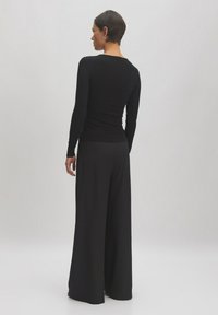 Langärmliges schwarzes Rippenoberteil, kombiniert mit weiten schwarzen Hosen. Das Design ist schlank, tailliert und weist durchgehend glatte Texturen auf.