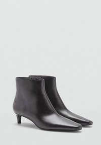 Bottines en cuir noir avec un bout pointu, un talon kitten et une finition lisse. Dispose d'une fermeture éclair sur un côté.