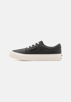 Zwarte synthetische sneakers met witte rubberen zolen, voorzien van witte veters en een subtiel logo op de zijkant. Ronde neus en laag model.