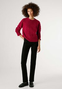 Κόκκινο πουλοβεράκι με υφή και σχέδιο ζιγκ-ζαγκ, άνετη εφαρμογή και ριμπ γιακά; συνδυασμένο με εφαρμοστά μαύρα παντελόνια και μαύρα παπούτσια.