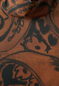 Tela marrón con intrincados patrones negros de remolinos y formas. La textura es suave, resaltando el contraste audaz del diseño.