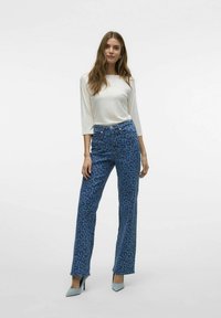 Blauwe luipaardprint jeans met een hoge taille en wijde pijpen, gecombineerd met een crèmekleurige langermige top en lichtblauwe puntige hakken.