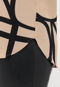 Top beige con un motivo astratto nero, con una finitura testurizzata e un orlo arrotondato. Abbinato a un fondo simile pelle nera.
