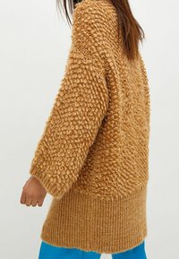 Flauschiger Strickpullover in Senfgelb, mit strukturiertem Boucle-Muster, weiten Ärmeln und geripptem Saum. Weiches Material, gemütliches Design.